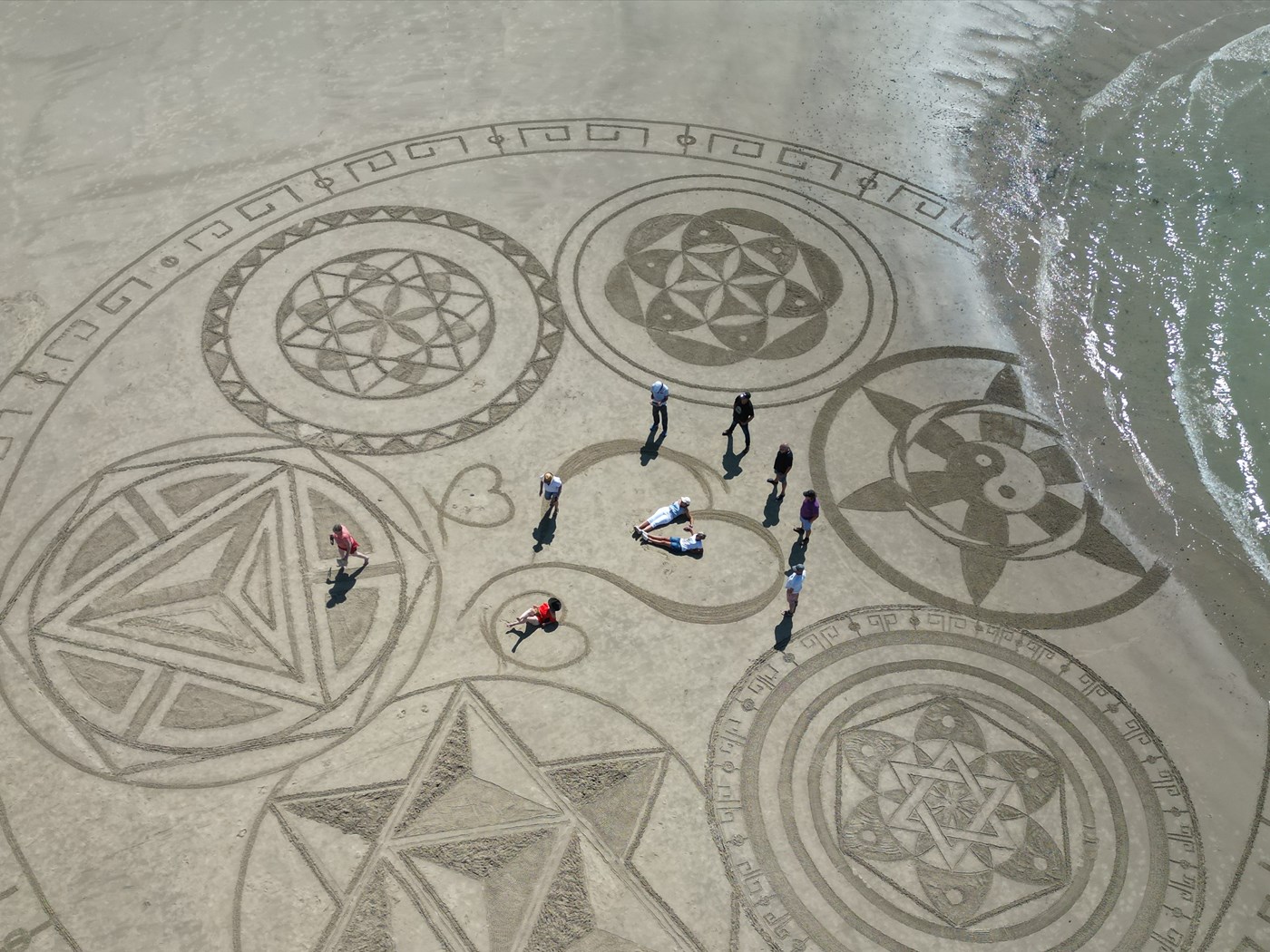 Participants au cœur d’une grande création collective tracée dans le sable au bord de la mer