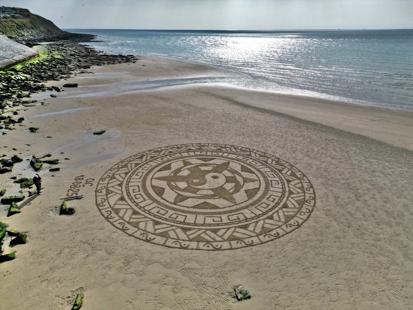 Grand mandala tracé sur le sable au bord de la mer